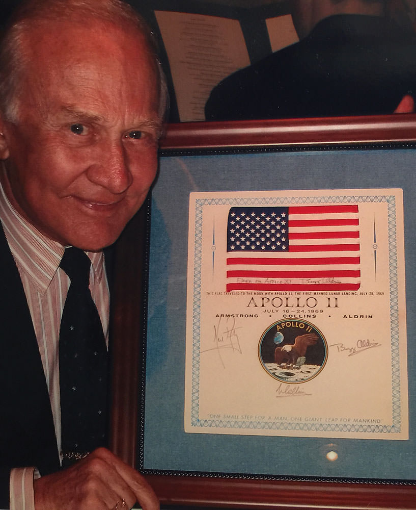 Apollo 11 astronaut Buzz Aldrin holding a flown US flag presentation signed by the entire crew, plus his additional autograph on flag itself. Sold by RR Auction.